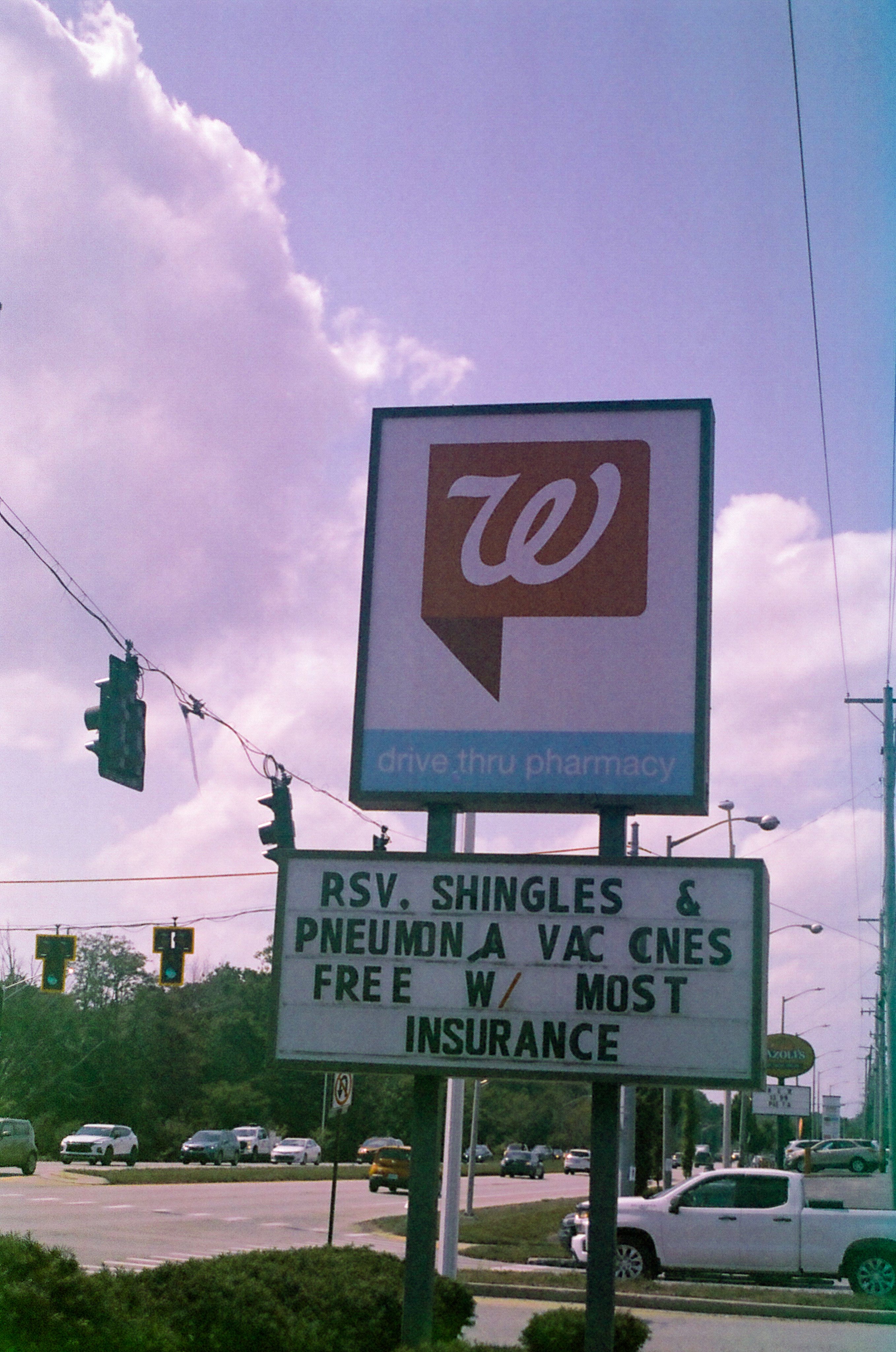 Photo of a Walgreens pharmacy sign on a street corner. Below the logo is a sign reading "RSV. SHINGLES & PNEUMONIA VACCINES FREE W/ MOST INSURANCE"